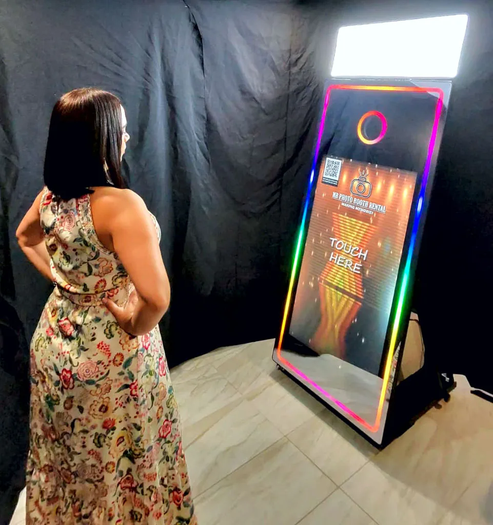 Smiling woman taking a photo in front of the mirror photobooth with glowing screen